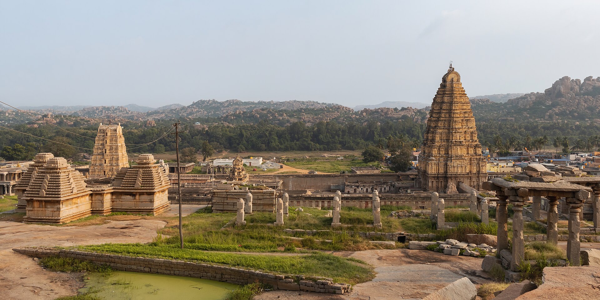 The wide-angle view of the Galigopuram of the Virupaksha Temple in Hampi captured from Hemakunta Hill complex. The photograph showcases the Gopuram's towering height and elaborate carvings, which depict various mythologi