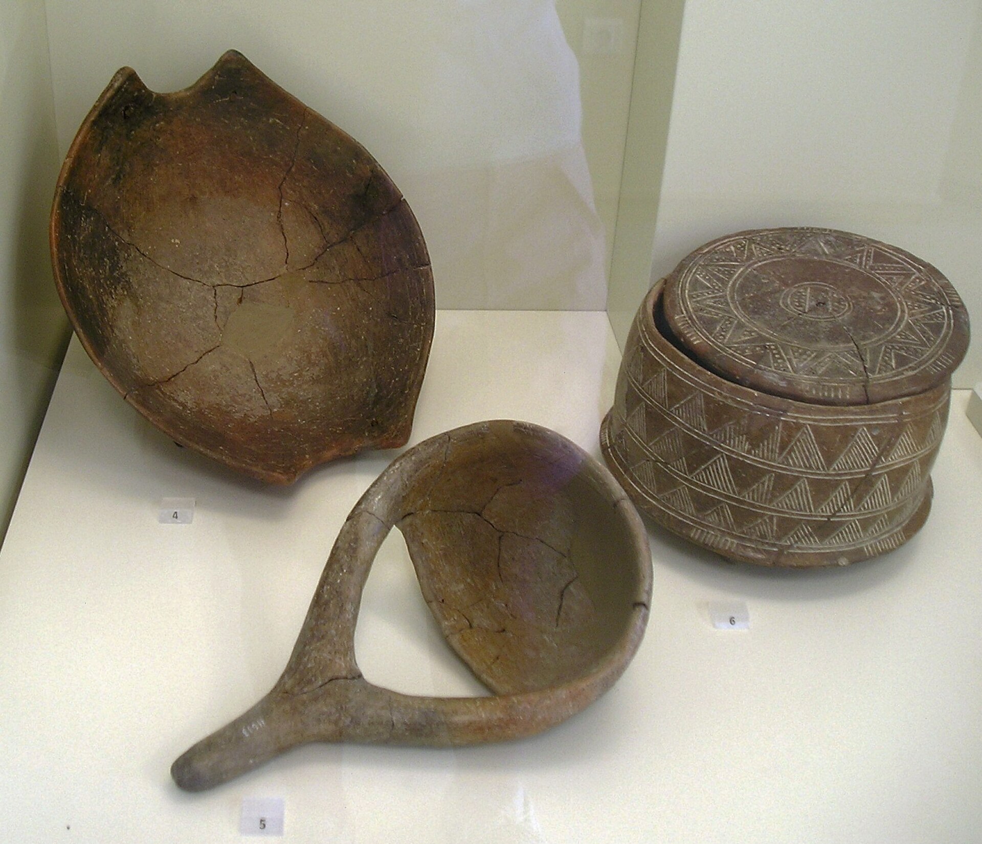 (4) Bowl with fork handles, pottery. Knossos, Early Neolithic, 6500-5800 BC. (5) Ladle, pottery. Knossos, Late Neolithic, 5300-4500 BC. (6) Three-legged vessel with lid and engraved decoration. pottery. Knossos, end of N
