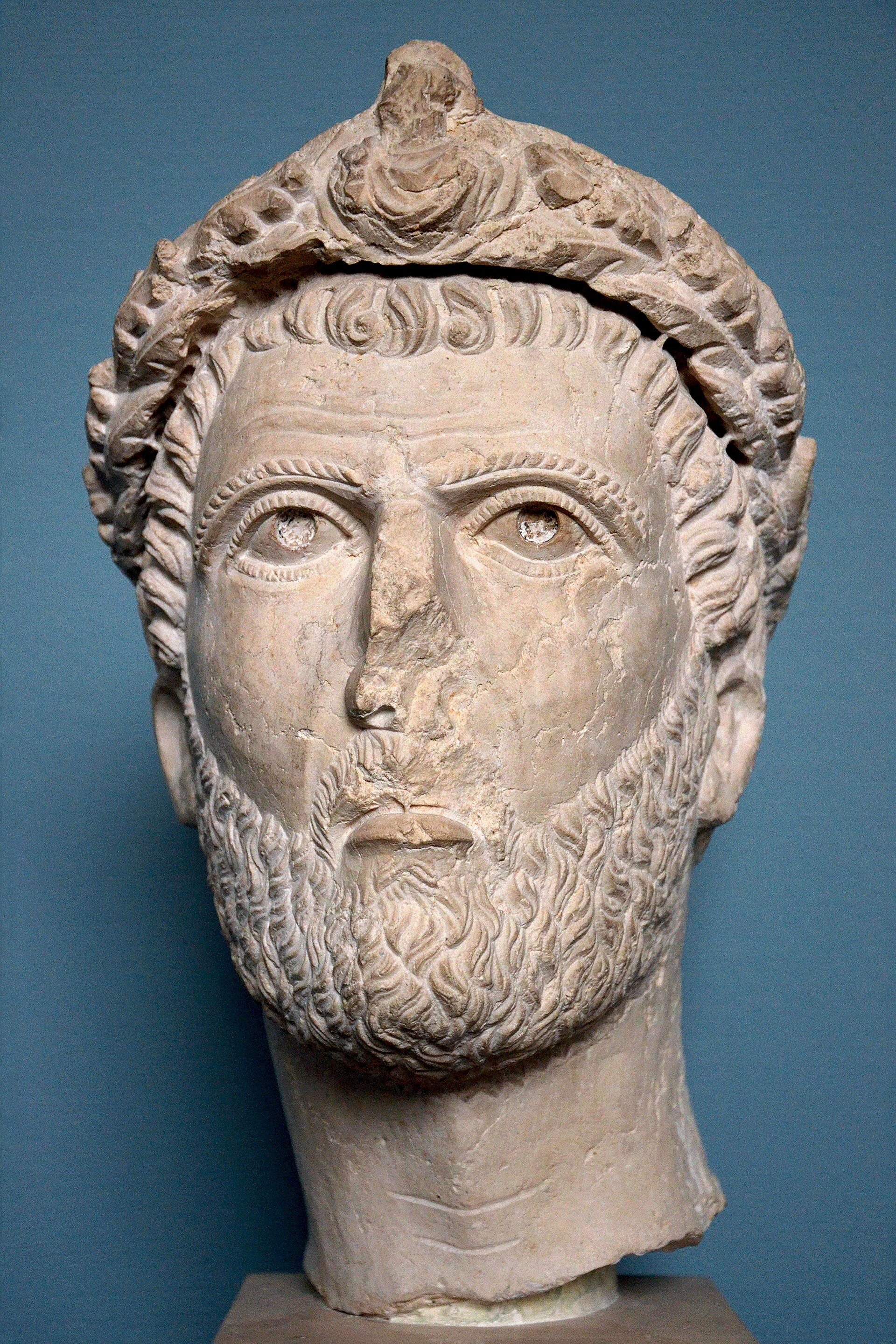 Limestone portrait of a leading Palmyrene, c. 230-250 AD, Ny Carlsberg Glyptotek, Copenhagen. An oak wreath with a small bust at its centre crows this powerful statue head. The unfinished back shows that the statue stood